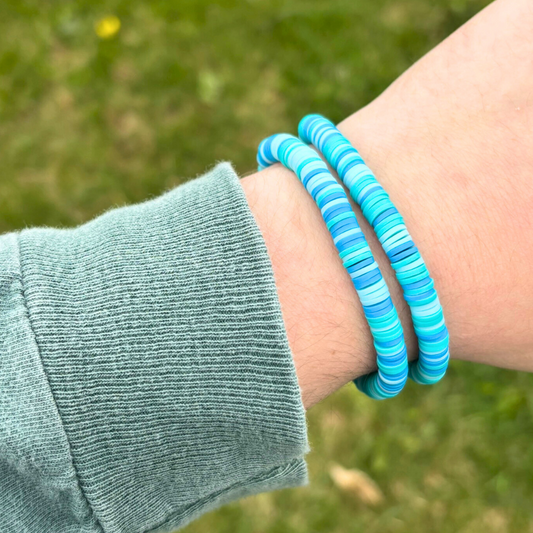 Person wearing two blue striped bracelets on a grassy background